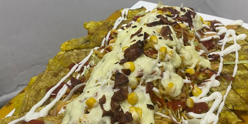 Patacones cubiertos de queso fundido, tocineta, maíz tierno y salsas