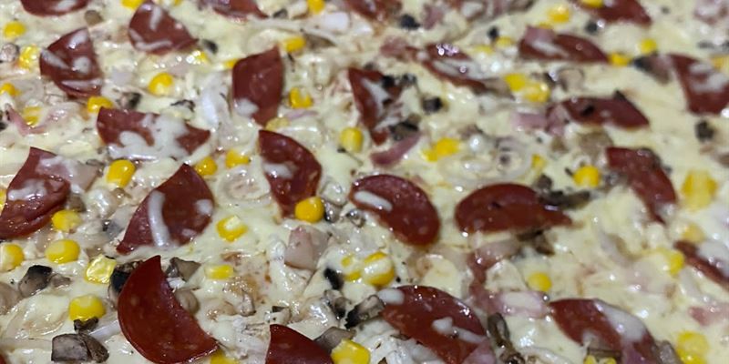 Pizza cubierta de queso fundido con peperoni, maíz tierno, champiñones y jamón